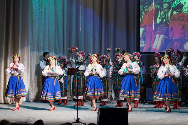 Dancers of the Bukovyna Ensemble performing on stage in embroidered blouses, blue skirts and floral headdresses