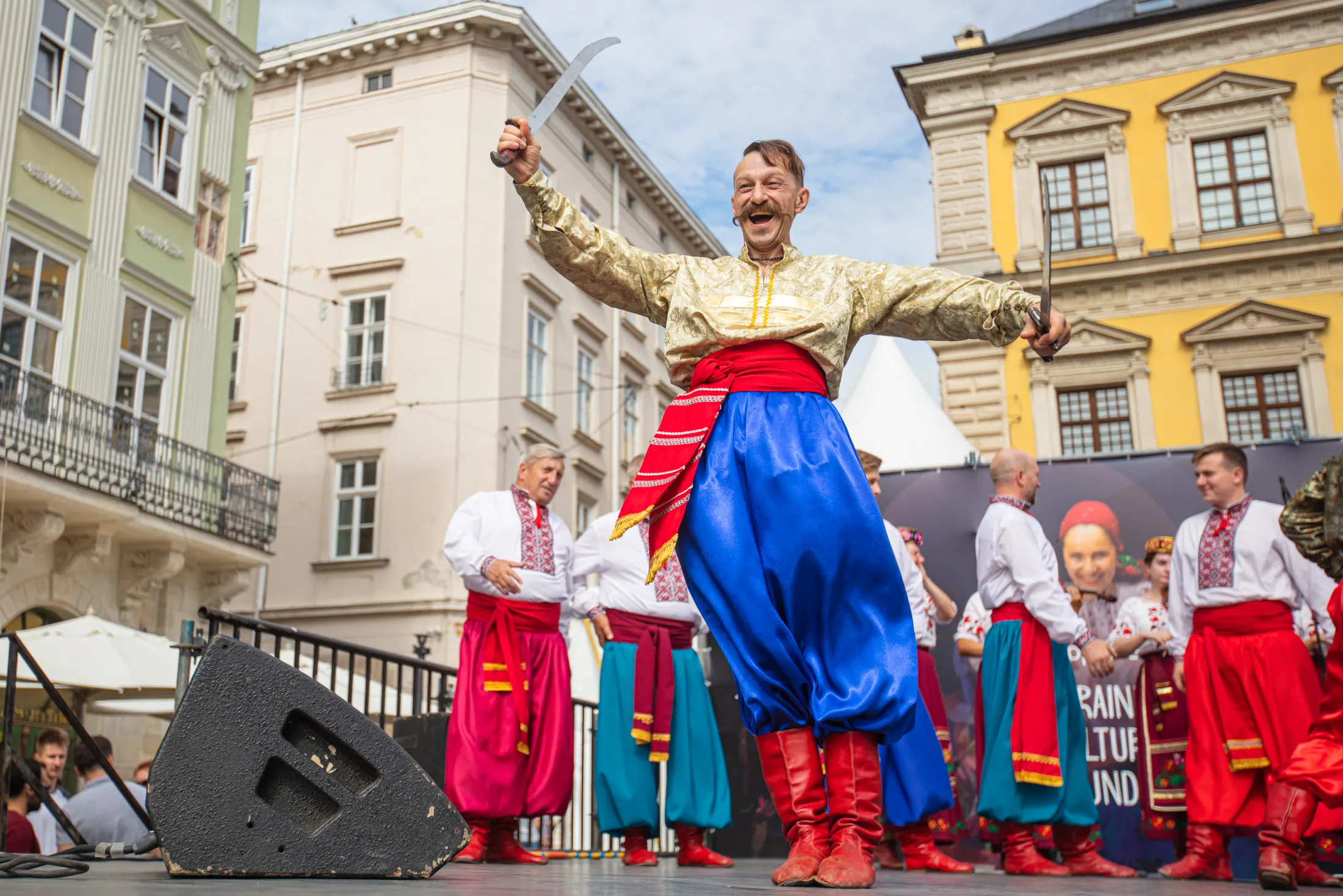 A Cossack dancer in gold and blue costume performing with sabres in a historic Lviv square